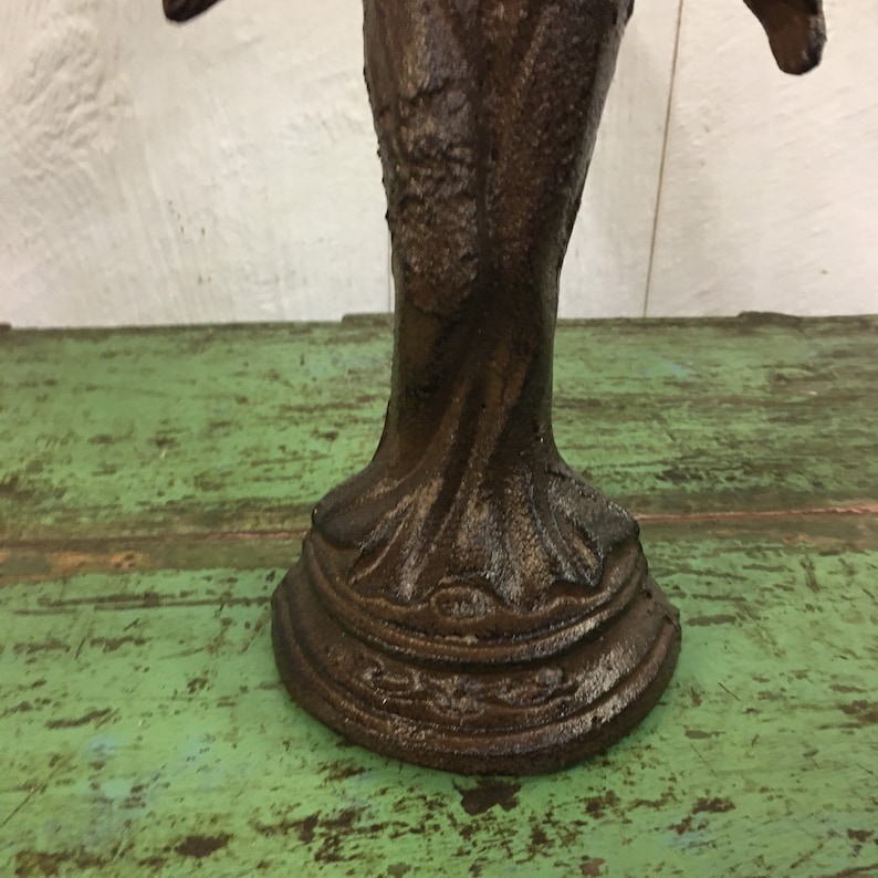 May include: A dark brown cast iron bird sculpture with intricate details. The bird is perched on a base with a decorative design.