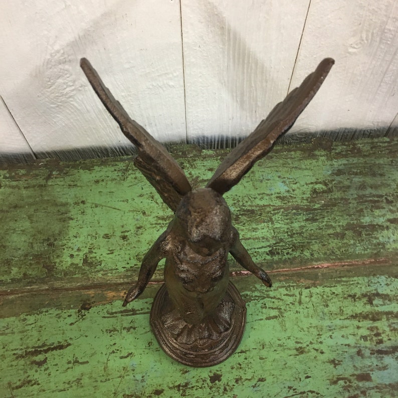 May include: A cast iron angel figurine with outstretched wings. The angel is standing on a round base and is painted in a dark brown color.
