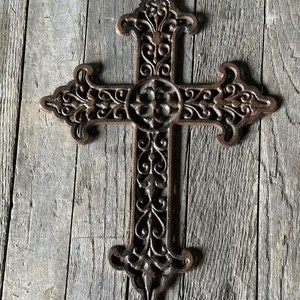 May include: A large, ornate, cast iron cross with a brown finish. The cross is decorated with intricate scrollwork and floral designs.