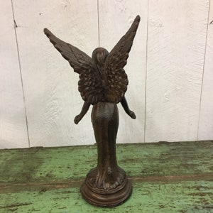 May include: A brown cast iron angel statue with wings outstretched. The angel is standing on a round base.