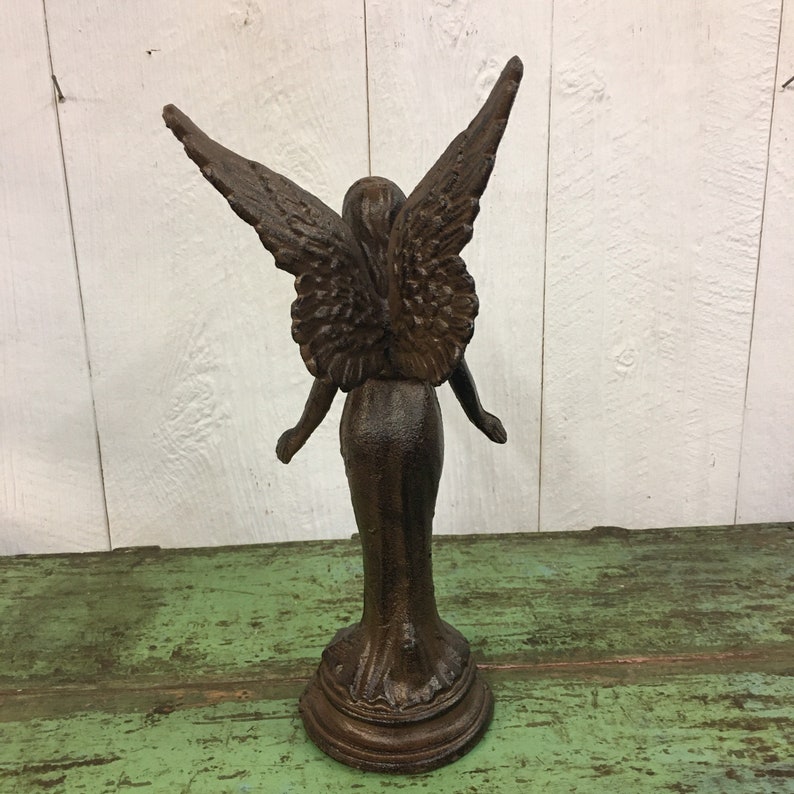 May include: A brown cast iron angel statue with wings outstretched. The angel is standing on a round base.