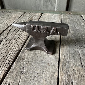 May include: A small, cast iron anvil with a rounded top and a flat base. The anvil is marked "U.S.A." on the side.