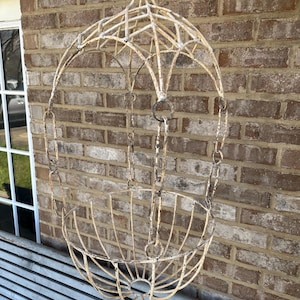 May include: A white metal hanging planter with a decorative arched top and a round basket. The planter is hanging from a chain.