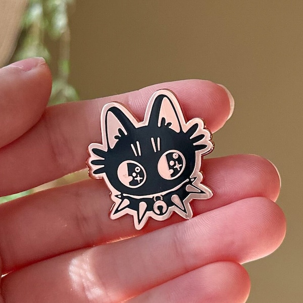 May include: Black and white enamel pin of a cat with a spiked collar and large eyes. The pin is rose gold colored.