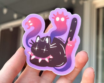 Puede incluir: Un gato negro con un collar de pinchos y ojos brillantes está rodeado de tres fantasmas rosas y morados. Los fantasmas tienen ojos grandes y son de diferentes formas. La pegatina está sobre un fondo morado y tiene la palabra "CAMCAT" escrita en ella.