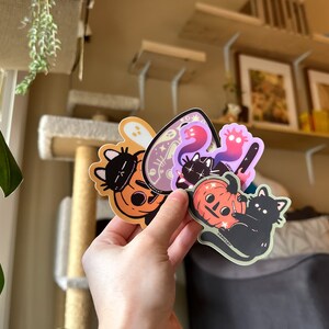 Pode incluir: Um conjunto de cinco adesivos tem&aacute;ticos de Halloween com gatos pretos, ab&oacute;boras e fantasmas. Os adesivos s&atilde;o impressos em vinil transparente e t&ecirc;m um acabamento brilhante.