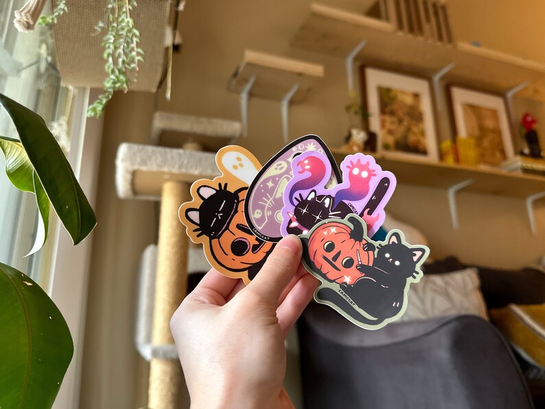 Pode incluir: Um conjunto de cinco adesivos tem&aacute;ticos de Halloween com gatos pretos, ab&oacute;boras e fantasmas. Os adesivos s&atilde;o impressos em vinil transparente e t&ecirc;m um acabamento brilhante.