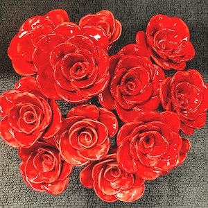 May include: A cluster of ten red ceramic roses, each with a glossy finish, arranged in a heart shape.