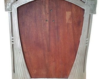 May include: A silver-toned picture frame with an Art Deco design. The frame has a wood backing and a beveled edge.