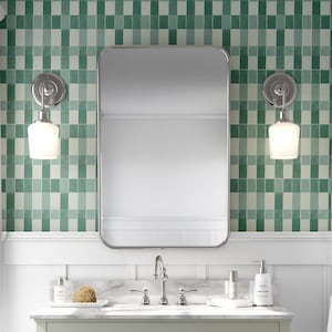 May include: A white bathroom vanity with three drawers and a bottom shelf. The vanity has a white marble countertop with a chrome faucet and two chrome sconces with white glass shades. The bathroom has green and white checkered wallpaper.