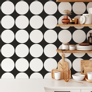 May include: A kitchen with white cabinets and a white countertop. The backsplash is black with large white circles. There are wooden shelves with various items on them.