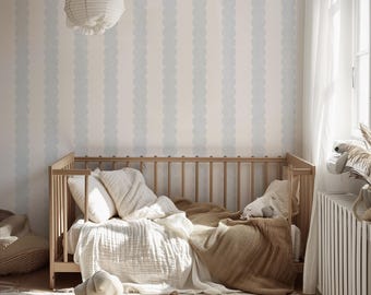 May include: A wooden crib with vertical slats, dressed in white and tan bedding, positioned against a wall featuring light blue and white scalloped vertical striped wallpaper. A white paper lantern hangs above the crib in a room with a rug.