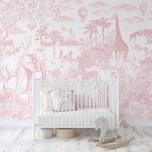 May include: A white crib with a pink safari-themed wallpaper background. The wallpaper features illustrations of elephants, giraffes, zebras, and hot air balloons. A pillow with "good night" text and a wooden rocking horse are in the foreground.