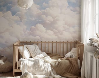 May include: A light-colored wooden crib with white and tan bedding, positioned against a wall featuring a mural of fluffy white clouds in a blue sky. A white paper lantern hangs above, and wooden toy vehicles sit on a textured white rug.