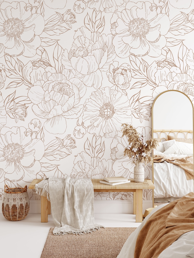 Puede incluir: Un interior de dormitorio con una pared blanca con un patr&oacute;n de papel tapiz floral en marr&oacute;n. El papel tapiz tiene un patr&oacute;n repetitivo de grandes peon&iacute;as y hojas. La habitaci&oacute;n cuenta con un banco de madera con una manta blanca, una cesta de mimbre, un espejo y una cama con una manta marr&oacute;n.