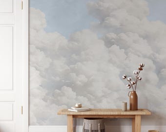 May include: A wall mural featuring a soft, painterly sky filled with voluminous white and light gray clouds against a pale blue background. The scene is set behind a wooden bench holding a brown vase with cotton stems and a woven basket.