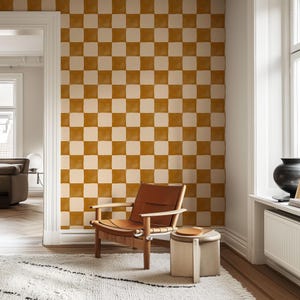 May include: A room with a checkered wallpaper in shades of brown and white. A brown leather chair sits in front of the wall, with a small round stool in front of it. The room has a large window with white trim.