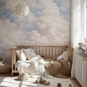 May include: A wooden crib with a white and beige bedding set. The crib is in a room with a white cloud wallpaper and a white lamp hanging from the ceiling.
