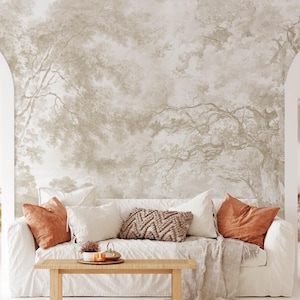 May include: A living room scene featuring a white sofa adorned with decorative pillows in shades of white, rust, and brown. A wooden coffee table holds a tray with a small plant and decorative items. The backdrop is a mural depicting a forest scene.