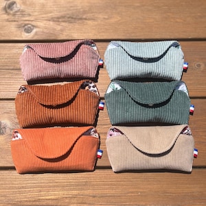 Peut inclure: Six pochettes rectangulaires en velours côtelé disposées en deux colonnes. Les pochettes sont rose poudré, bleu clair, orange brûlé, vert foncé, orange vif et beige. Chacune possède un rabat, une petite étiquette drapeau français et une doublure.
