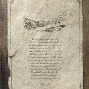 May include: A rectangular piece of textured, off-white paper with deckled edges featuring a black ink illustration of a desert landscape and the full text of the poem Ozymandias by Percy Shelley, framed by a thin black decorative border.