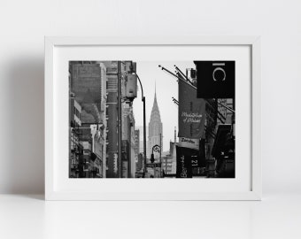 May include: A black and white photograph of a city street in New York City. The Chrysler Building is visible in the distance. There are signs for various businesses, including "Zocdoc", "Bershka", and "Marketplace of Makers".