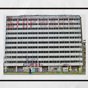 May include: A large, white building with many windows. The building is covered in graffiti, including the word "WAR" in large, red letters. The building is located in an urban area.