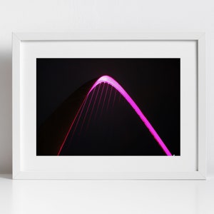Può includere: Primo piano di un arco di ponte illuminato da luci rosa brillanti contro un cielo notturno scuro.