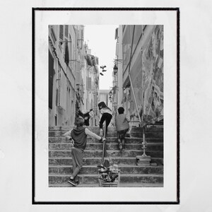 May include: Black and white framed photograph of children climbing a set of outdoor stairs in a narrow alleyway. One child leans on a metal railing, while two others ascend the steps. A shopping cart sits at the base of the stairs.