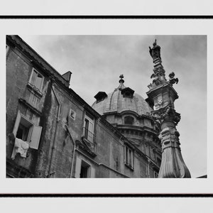 May include: A black and white photograph of a building with a dome and a statue on a column. The building has a weathered facade with windows and a stone dome. The statue is on top of a tall column with a decorative base.