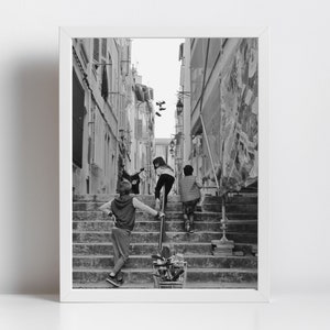 May include: Black and white framed photograph of children climbing a long set of outdoor stairs in a narrow European street. One child is leaning on a metal railing, while two others are ahead, ascending the steps. The scene is captured in natural light.