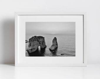 May include: Black and white photograph of two large rock formations jutting out of the ocean. The rocks are shaped like arches and are located near the shore. A small boat is visible in the distance.