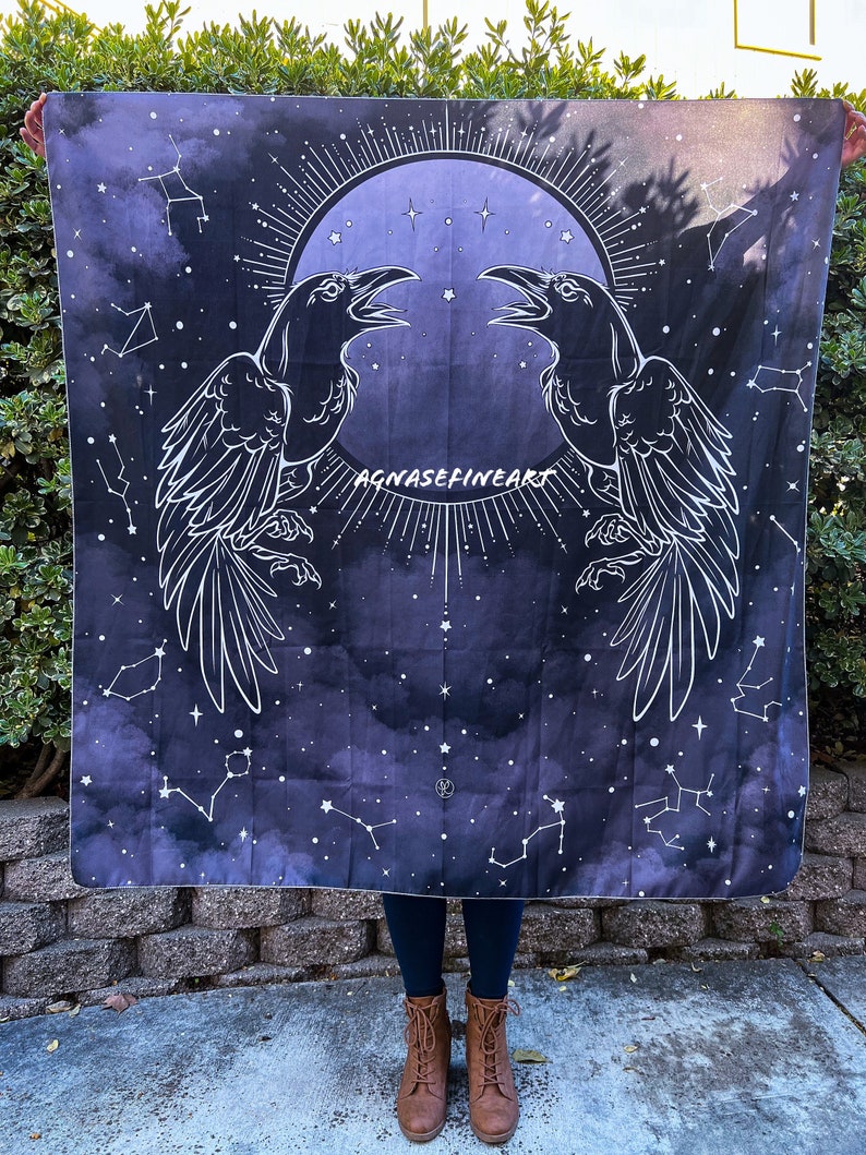 May include: A black and white tapestry with a dark blue background featuring two ravens facing each other with their wings spread. The ravens are outlined in white and have a moon and stars in the background. The text "AGNASEFINEART" is printed in white at the bottom of the tapestry.