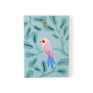 Könnte beinhalten: Eine hellblaue Keramikfliese mit einem gemalten rosa Vogel mit blauem Schwanz, der auf einem Zweig mit grünen Blättern sitzt.