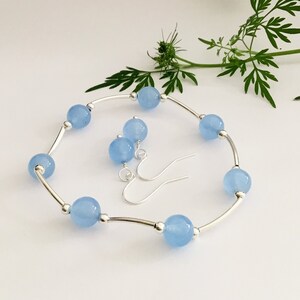 May include: A set of light blue gemstone earrings and a bracelet. The earrings are silver with a hook closure. The bracelet is silver with a curved bar design and light blue round gemstones.