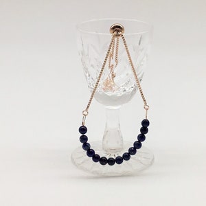 May include: A gold chain bracelet with a row of dark blue beads. The bracelet is displayed on a clear glass pedestal.