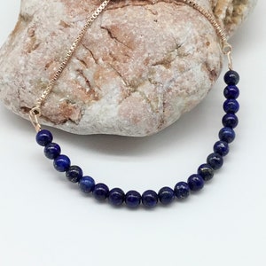 May include: A blue lapis lazuli beaded bracelet with a gold adjustable slider clasp.