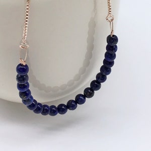 May include: A delicate bracelet made with dark blue lapis lazuli beads and a rose gold chain.