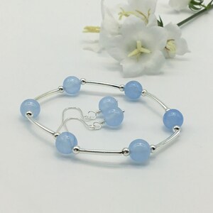 May include: A silver bracelet with light blue beads and matching earrings. The bracelet has a simple design with a silver bar connecting the beads.