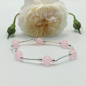 May include: A delicate bracelet with a silver chain and pink beads. The bracelet is displayed on a white background with a white rose.