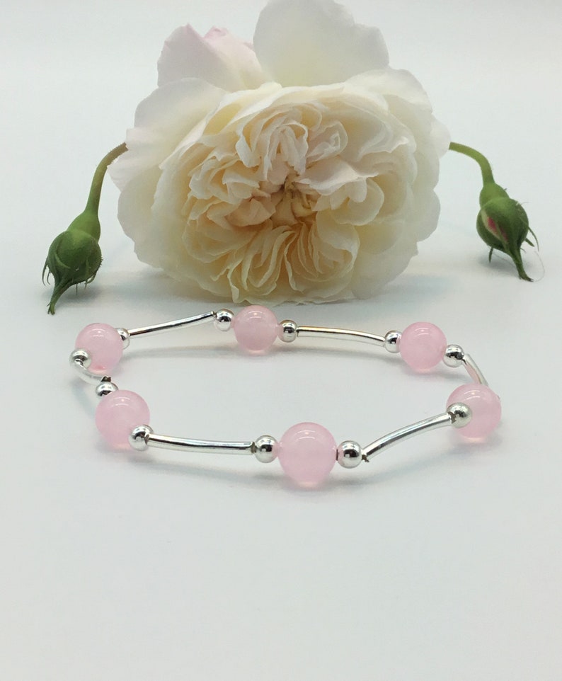 May include: A delicate bracelet with a silver chain and pink beads. The bracelet is displayed on a white background with a white rose.