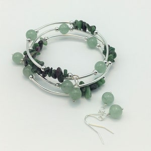 May include: A silver bracelet with green and pink stones, and matching earrings with green stones.