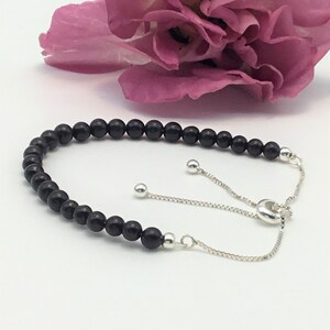 Peut inclure: Bracelet en perles noires avec un fermoir coulissant argenté réglable. Le bracelet est composé de perles noires rondes et d'une chaîne argentée.