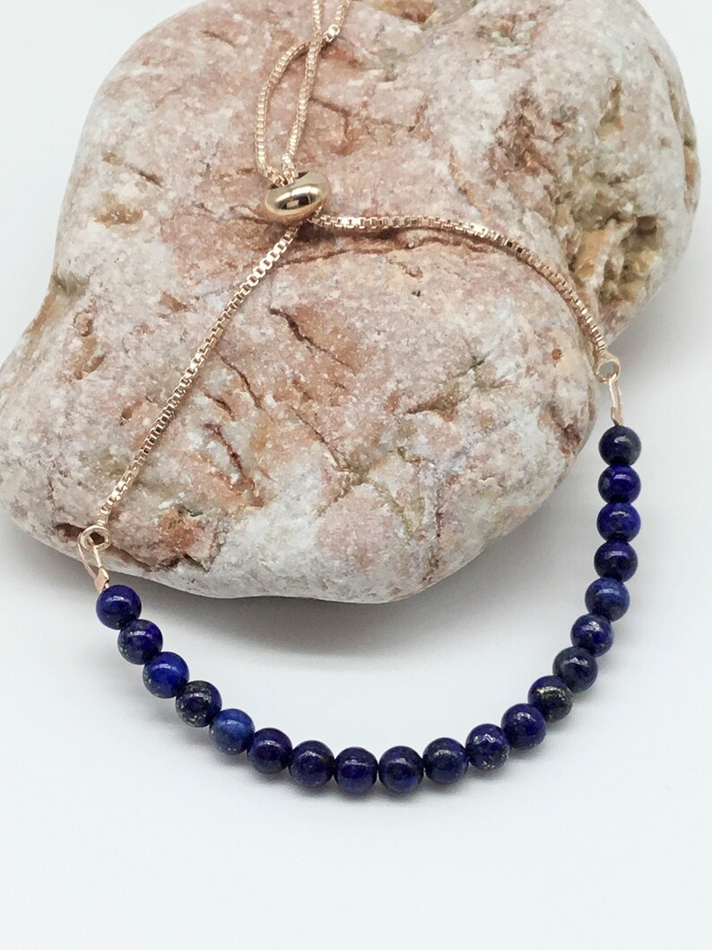 May include: A blue lapis lazuli beaded bracelet with a gold adjustable slider clasp.