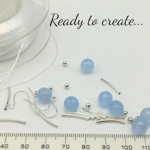 May include: A close-up of jewelry making supplies, including light blue beads, silver jump rings, and earring hooks. A ruler is visible in the bottom of the image, with measurements from 40 to 110. The text "Ready to create..." is visible at the top of the image.