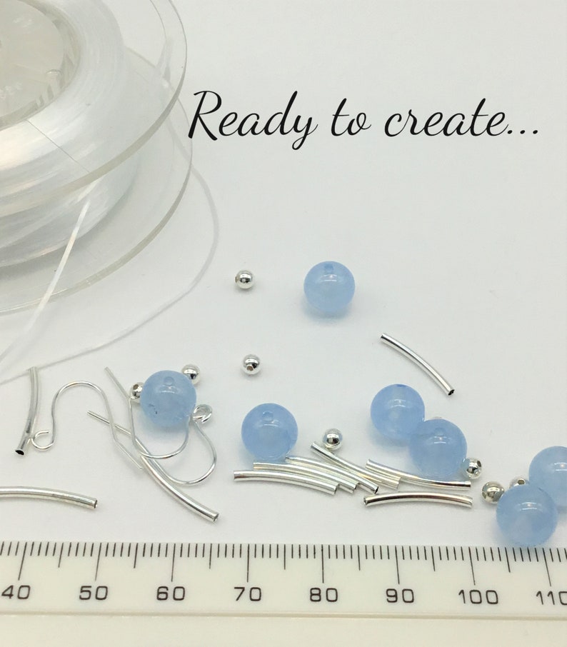 May include: A close-up of jewelry making supplies, including light blue beads, silver jump rings, and earring hooks. A ruler is visible in the bottom of the image, with measurements from 40 to 110. The text "Ready to create..." is visible at the top of the image.