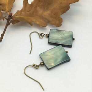 May include: A pair of square-shaped earrings with a green and white iridescent finish. The earrings are made of mother of pearl and have brass hooks.