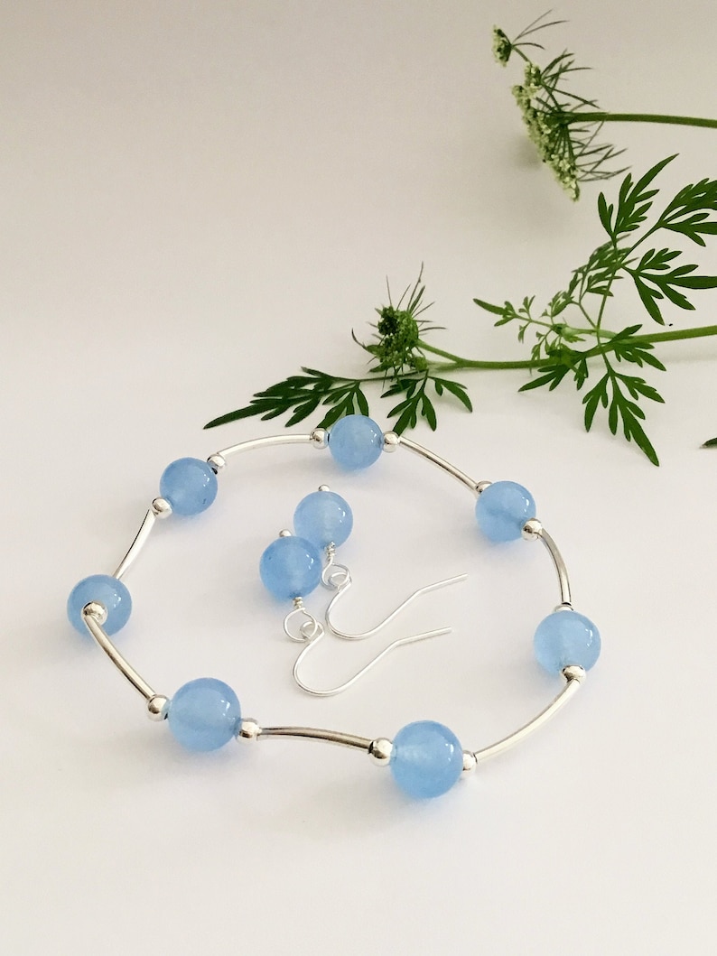 May include: A set of light blue gemstone earrings and a bracelet. The earrings are silver with a hook closure. The bracelet is silver with a curved bar design and light blue round gemstones.