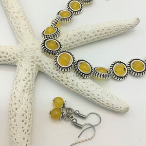 May include: A set of yellow gemstone jewelry with silver accents. The bracelet has a toggle clasp and the earrings are dangle style.