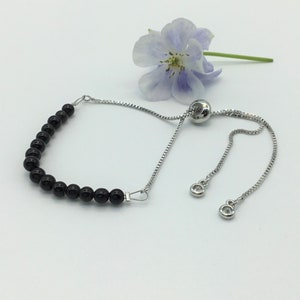 May include: A black bead bracelet with a silver chain and adjustable clasp. The bracelet is made of round black beads and a silver chain with a sliding clasp.